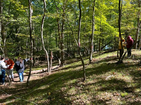 People standing in the woods, looking at trees labelled with pink flagging tape, with a grid marked out on the ground with measuring tapes. These are ESU Plant Ecology students surveying a permanent forest plot at Stony Acres, a nature preserve.