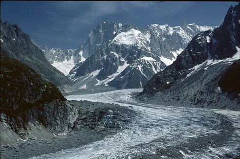 A glacier curving towards us with snowy mountains in the background. The blue sky has a bright clarity typical of high altitudes.