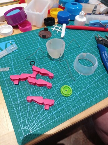 Two plastic caps, two clothespins and wire on a table. Lots of plastic waste in the background.