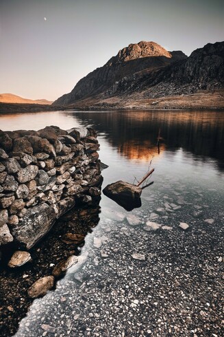 A winter moon rises over Tryfan and Llyn Idwal in Eryri. The light from the setting catches the top of the mountain. The lake is calm. The landscape is silent.