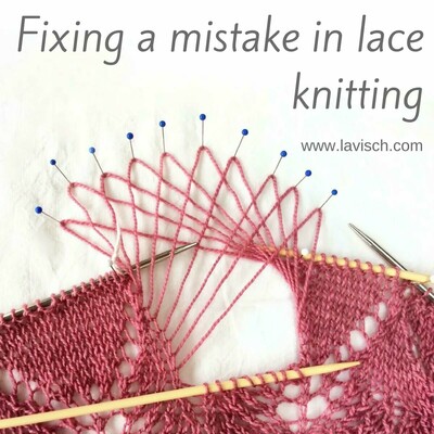 A partially ripped out lace edging in a pink knitted shawl, the strands are pinned out with blue pins.