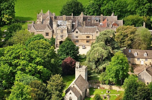 A huge castle with a lot of trees and grass in the background. The castle looks like a large hotel with a number of wings.