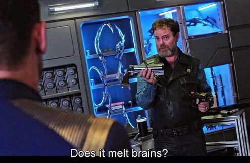 Dwight from the Office, but as a Star trek character, is standing and holding some kind of machine part. He's dressed in non Starfleet clothes, and also holding a phaser. He's standing in a room with lots of mechanical tubes and boards and tables. Closed caption reads, "Does it melt brains?"