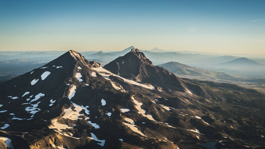 View of Middle and North Sister from the Summit of South Sister in Central Oregon. Glaciers and snow pocket the black volcanic landscape.