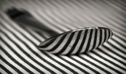 Black and white image of a spoon resting on stripy material.