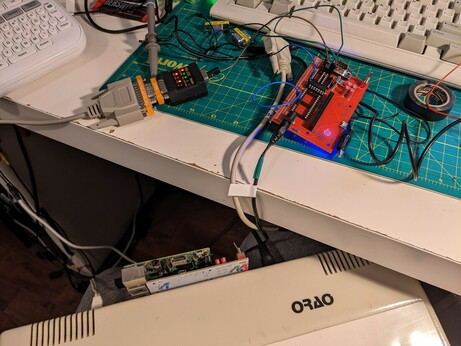 A bunch of wires and a red board connected to the white Orao computer, the computer is barely visible