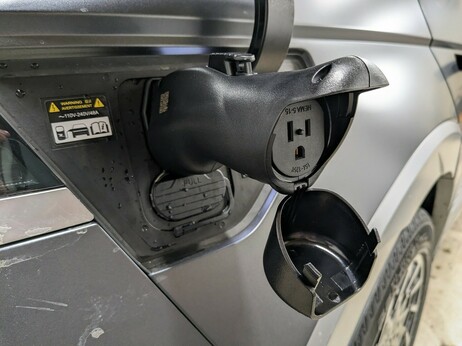 A close-up of the connector now plugged into the car's charge port, revealing the NEMA 5-15 household receptacle