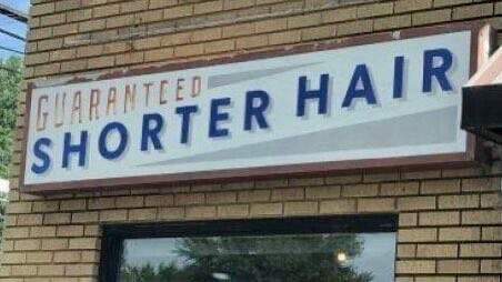 Business’s sign over window on brick building reads “Guaranteed Shorter Hair.”