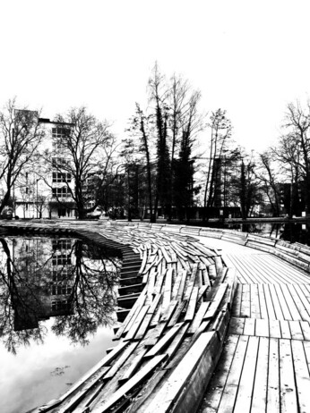 A curved wooden bridge by a block of flats in high contrast black and white