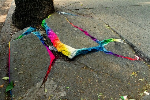 Photo of a cracked sidewalk, with the edges of the cracks painted in a rainbow of color. Photo by Alf A. Nieto, © Xomatok