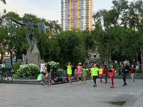 Zumba in the park. A group of Zumba enthusiasts are exercising, most of them middle-aged women. There are 2 elderly men.