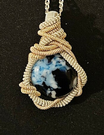 A wirewrapped pendant with gold/rose/silver wire twisted around a blue/black round glass cabochon