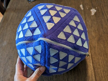 An icosahedron sewn from purple fleece that is about 16 inches in diameter and has a triangular grid of ten 3D printed triangles which covering each side.