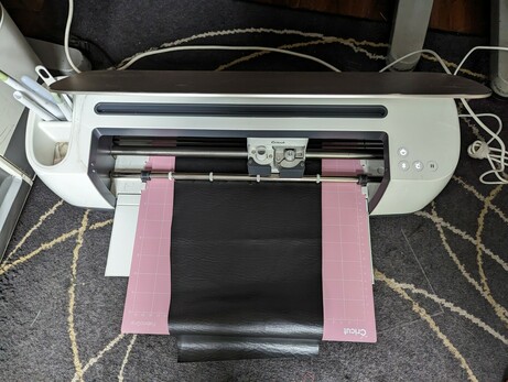 Black faux leather fabric on a pink cutting mat loaded into a Cricut vinyl cutter.