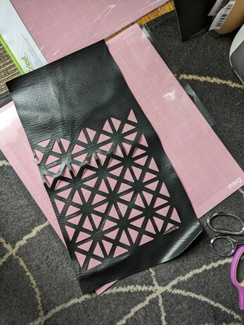 The same black faux leather fabric with a triangular grid cut out of it, resting on top of the pink mat.