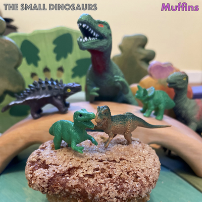 this is the single artwork for the song "muffins" by the small dinosaurs. it's a photograph of a jurassic-park-esque scene in which a bunch of toy dinosaurs are attacking a muffin and generally looking scary in the background