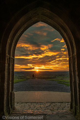 A person watching sunrise. View through the archway with golden clouds in the sky.