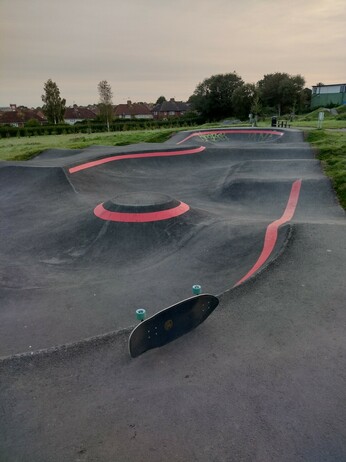 Photo of a BMX/skate pump track, with my board on its side in the foreground