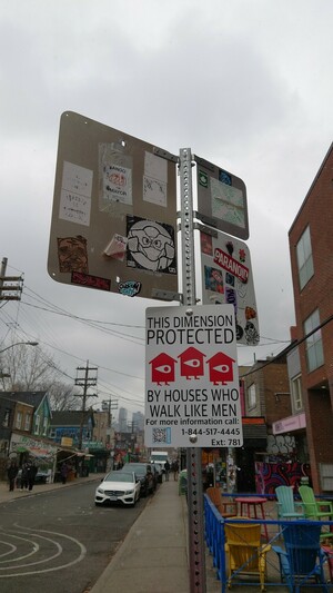 Sign bolted to a pole: "This dimension is protected by houses that walk like men"