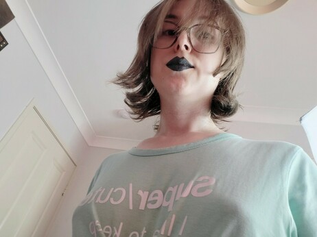 Selfie of Revy
She has short brown hair
Glasses and black lipstick with a silver tone
Shes looking down
The shape of her bøøbs can be seen through her shirt