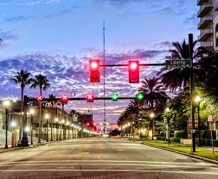 Late night / early morning view of a major downtown roadway, now ghostly empty yet brilliantly illuminated with traffic signals and street lights, beneath purple and blue cloudy skies.