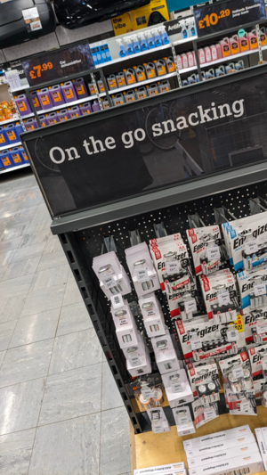 A convenience store display labeled "on the go snacking" that's stocked with various kinds of batteries