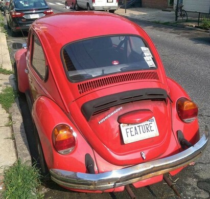 A photo showing the rear end of a red Volkswagen Beetle with a number plate that reads “FEATURE”