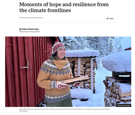 Screen capture and crop of BBC article "Moments of hope and resilience from the climate frontlines."

A photo depicts a woman in a sweater and holding a split log of firewood, in front of a red barn and shelters containing more firewood in stacks. Deep snow indicates the season.