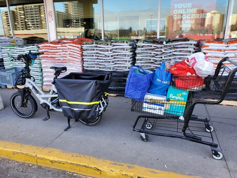 My cargo bike beside a shopping cart full of grocery bags and boxes