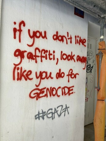 "If you don't like graffiti, look away like you do for genocide" written on a wall with red spray paint