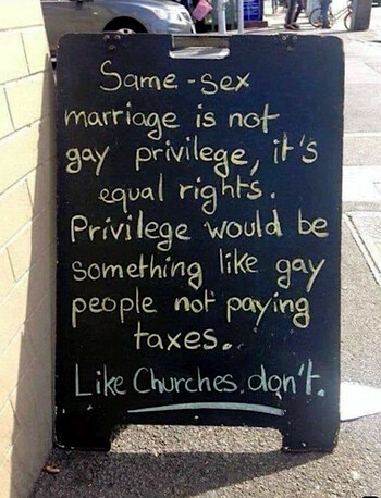 A black sandwich-board on a sidewalk, next to an outside building wall, displays the following message, written in chalk: 
"Same-sex marriage
is not gay privilege,
it's equal rights.
Privilege would be
something like gay people
not paying taxes.
-- Like churches don't."