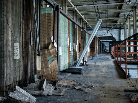A long elevated walkway. On the right are columns and railing, and on the left are rows of huge cardboard sheets with holes punched in them, hung vertically