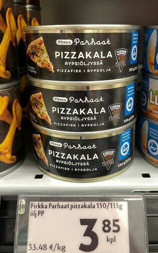 Nærbilde av tre hermetikkbokser med pizzakala rypsiöljyssä, eller pizzafisk i rypsolja, som det hete på svensk. Boksen e lav og rund, med et papirbånd rundt, kor bunnfargen e i svart, og det e illustrert med et foto av et pizzastykke på den ene sida og en illustrasjon av et pizzastykke på andre sida. Merket e Pirkka, som e K-market sitt butikkmerke.