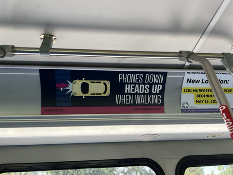 A advertisement from the Tennessee Highway Safety Office that says “phones down heads up when walking”