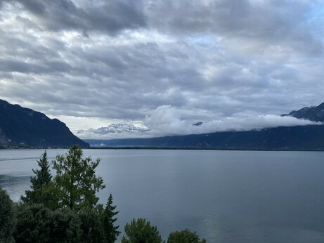 Photo looking out across a lake towards the slightly snowy mountains in the background that are shrouded by grey clouds.