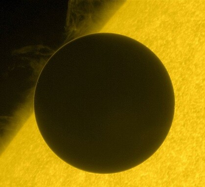 A dark, round silhouette of a planet partially obscures a bright yellow, textured background. The planet's edge appears slightly illuminated on the upper left side, creating a thin glowing outline.
