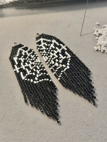 A pair of spiderweb beaded fringe earrings on a grey bead mat