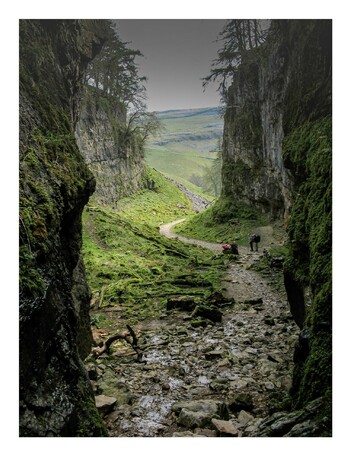 A photo of Trow Gill in the Yorkshire dales. Steep rocky sides with a winding path below and some walkers on the extreme right.