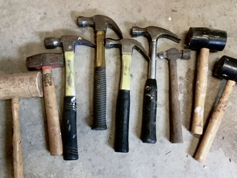 An assortment of hammers arranged artistically, like a bouquet, on a gray concrete floor: framing, claw, rubber mallet, lump hammer, ball peen, wooden mallet...
