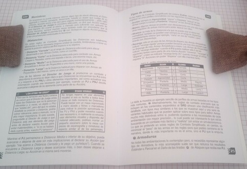 Foto de un ejemplar físico de la BETA preliminar de "Zodiac 2.5: System Reference Document". Abierto sobre las páginas 24 y 25, donde se explican la mitad de las reglas de "combate simplificado". Entre otros elementos puede verse una tabla de armas muy minimalista.