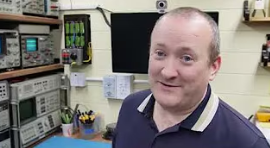 video image capture of youtuber Mend It Mark. A balding sort of middle-aged white man in a blue shirt smiles at the camera. Behind him are racks of electronic test gear sitting on a workbench