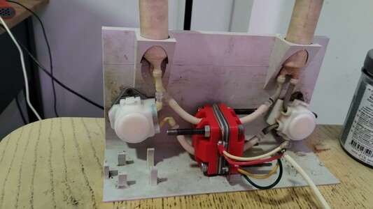 Flow battery test cell with peristaltic pumps. Red plastic cell around white tubing and hardware