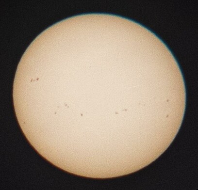 A projected image of the Sun at 13:45 UTC on 4 January 2025, taken with my iPhone. There are many sunspots on the surface and some green and red chromatic aberration around the edges.