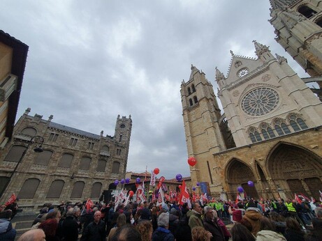 imagen de manifestación en la Plaza de Regla de León. Se ve el palco con numerosas banderas de León y sindicatos, con gente delante. De fondo, la catedral y el edificio de oficinas de la Diputación, con una torre.