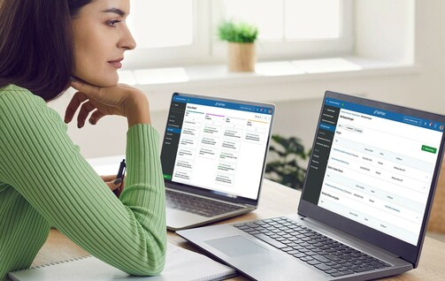 Woman sitting at desk in front of two screens, one showing OpenProject's meetings module, one showing OpenProject's boards module