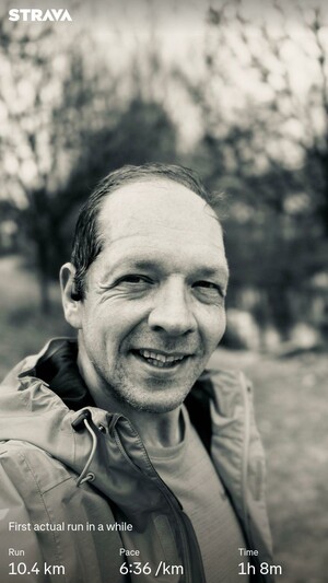 Me smiling into the camera in a close-up selfie, wearing a gray jacket. The background shows a blurred outdoor scene, possibly a park. Text overlay includes running statistics: 10.4 km run at a pace of 6:36/km, completed in 1h 8m.