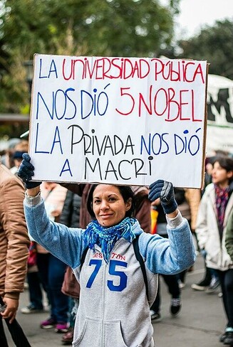 Persona en una marcha sosteniendo un cartel que dice: "La universidad pública nos dio 5 Nobel. La privada nos dio a Macri".