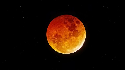 A red & orange full “blood” moon with stars in the background. From the March 13, 2025 Lunar Eclipse.