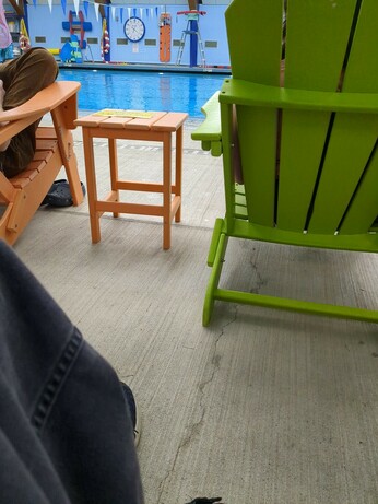 Low angled POV shot of the local pool. A geeen Muskoka chair dominates the foreground