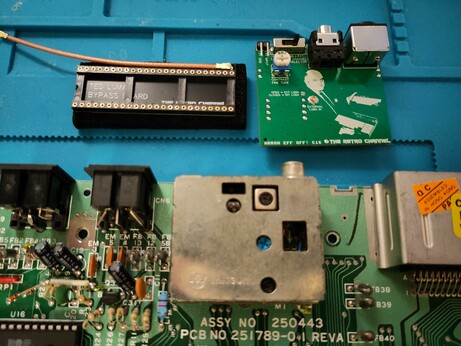 A Commodore 16 motherboard laid on a blue soldering mat, with the original modulator and the new replacement shown next to it, including a luma bypass board and a shielded wire, that will go into the TED socket. This helps to improve the video quality even further.